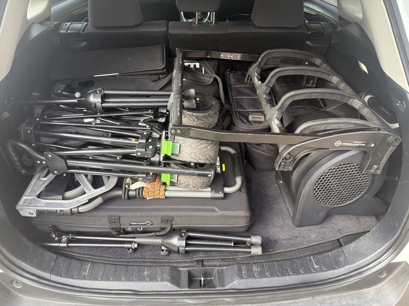 The trunk loaded: folding cart and wagon on top of the flat case, mic stand along the back edge, bags on the left, wedge on the right.